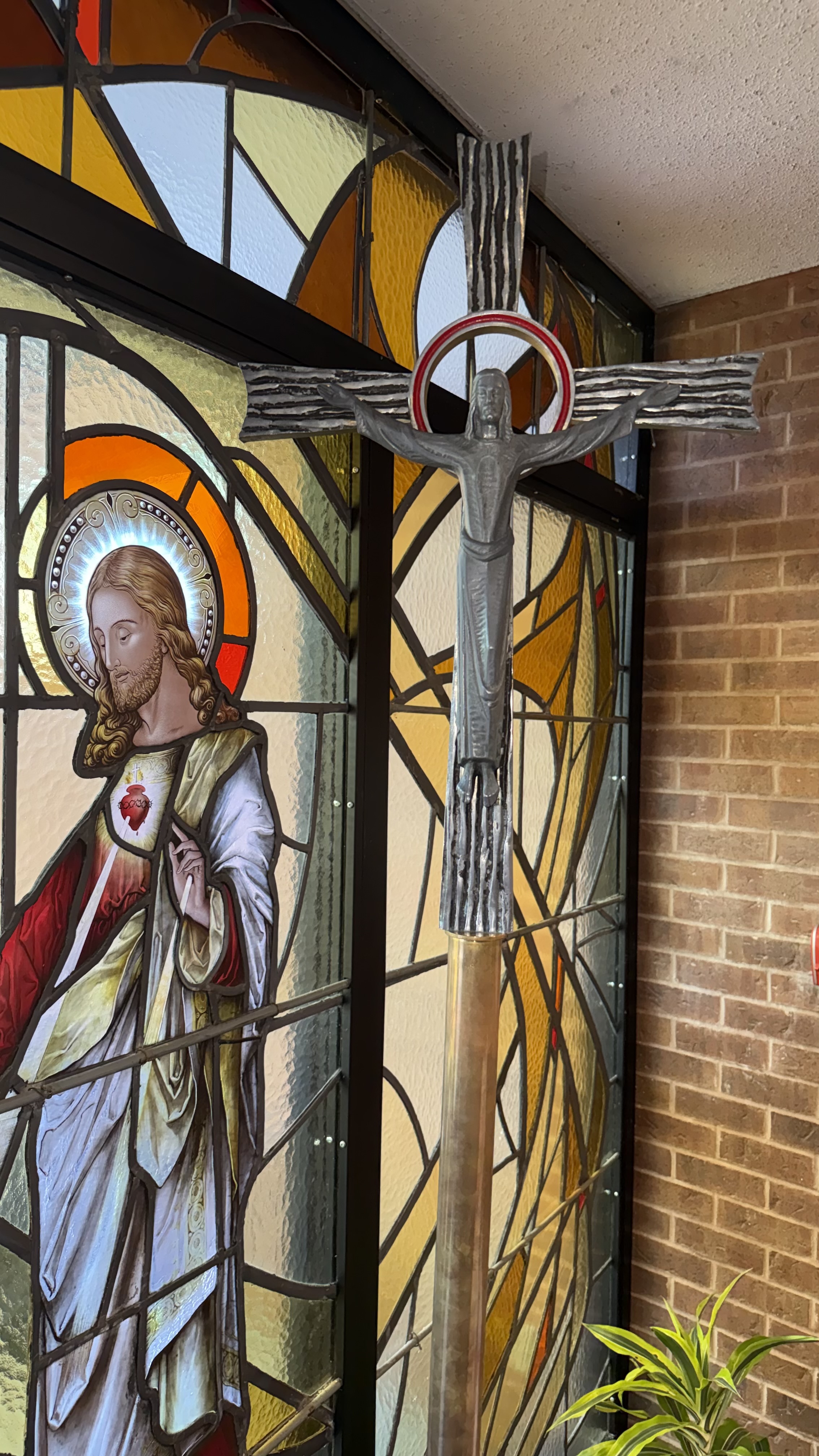 A picture of the Parish Processional Cross, next to a stain glass window of Jesus