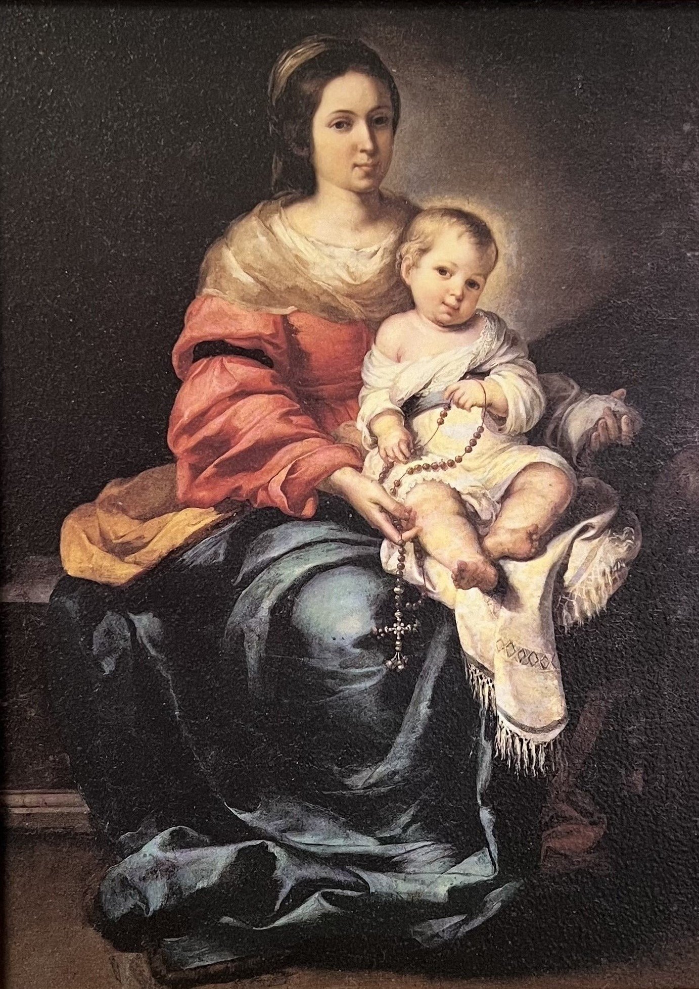 A painting of the Virgin Mary with Baby Jesus on her lap, as she holds a rosary in her hands
