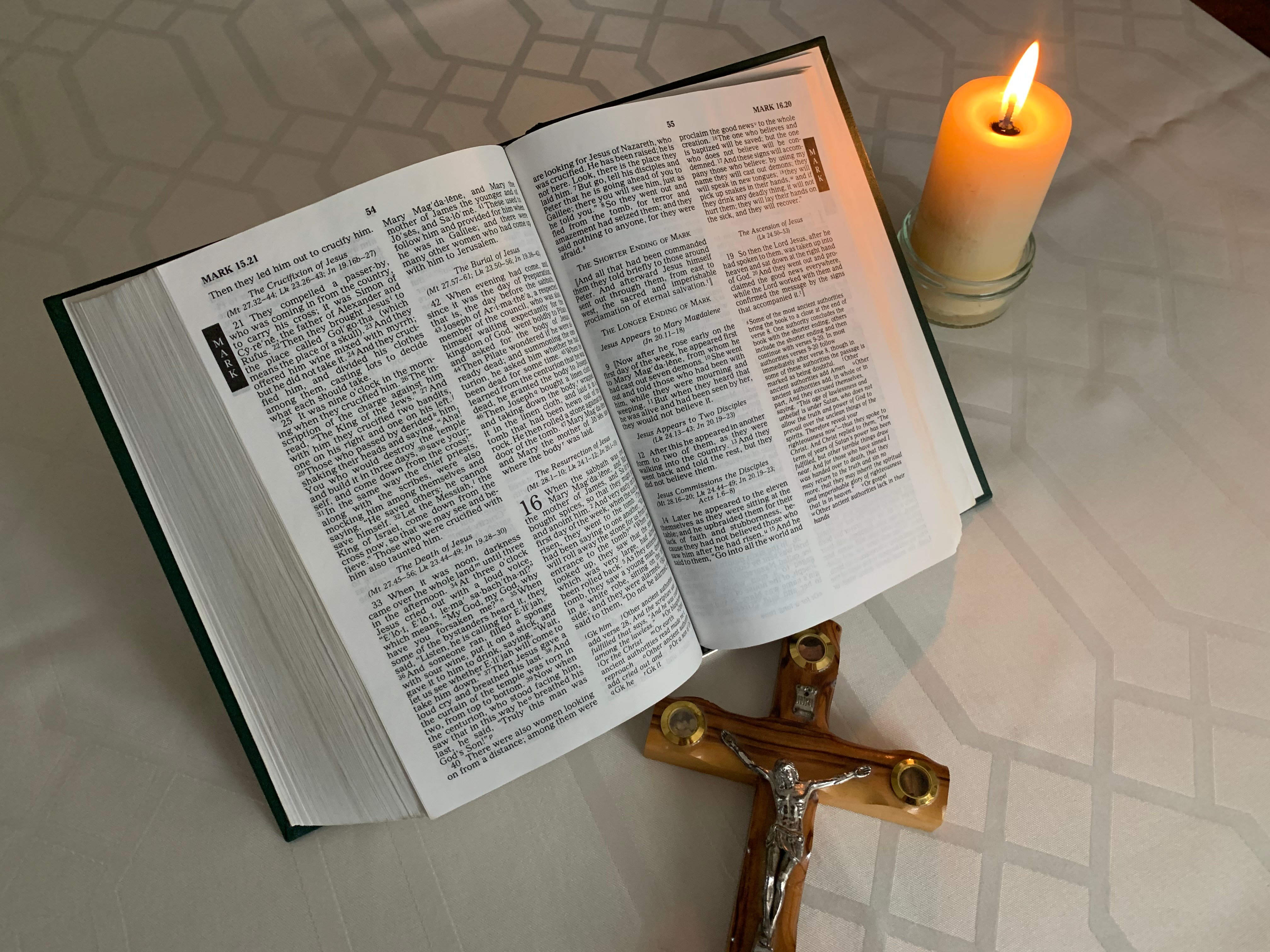 An image of a bible, together with a lit candle and a cross